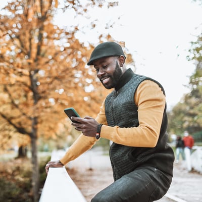VoIP Business Phones Thumbnail Photo of a smiling man standing outdoors. He is looking at something on his phone.